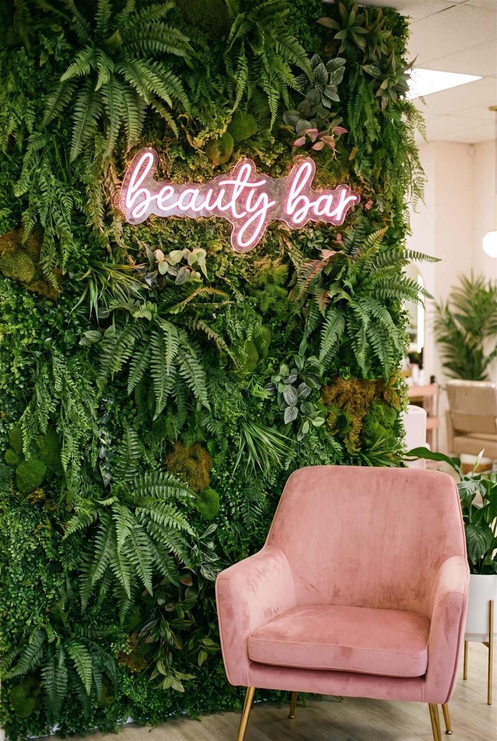 Pink beauty bar LED neon sign on a greenery wall above a pink velvet chair in a beauty salon (visualisation)